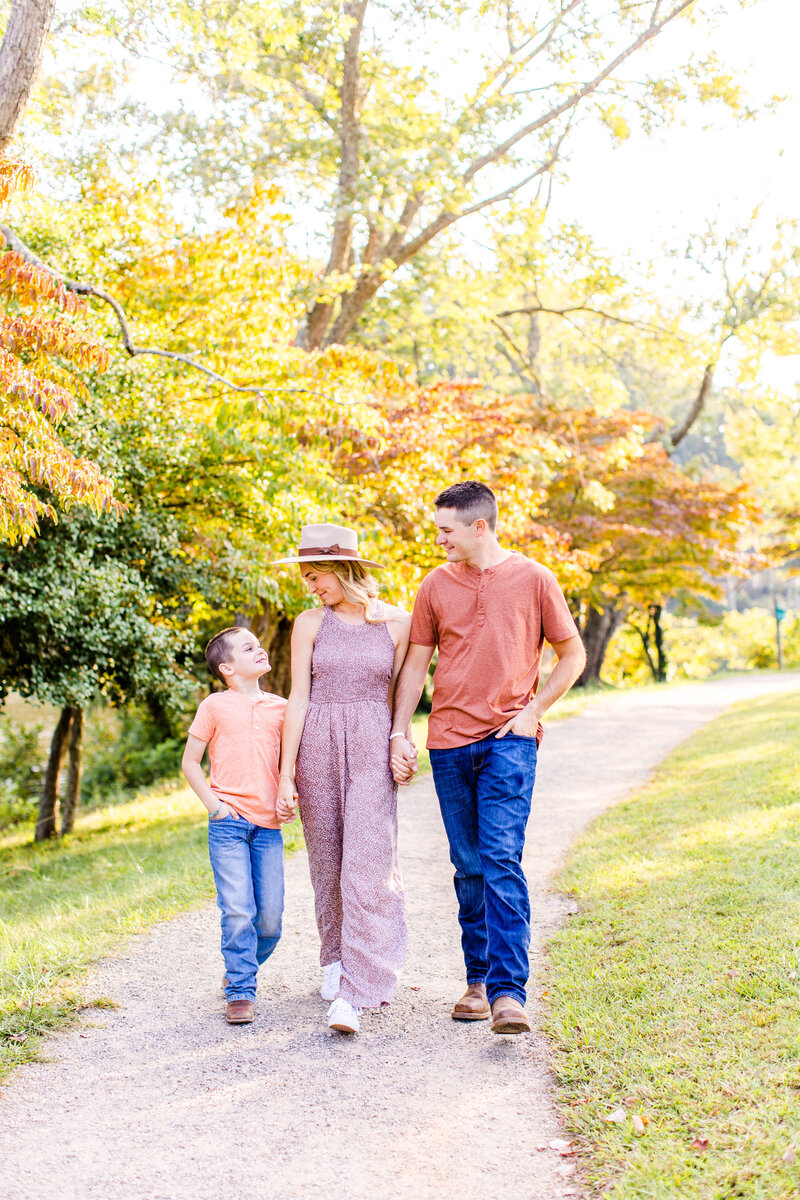 family of three walking together with fall leaves behind them