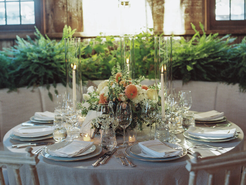 white linen semi-circle booth for wedding reception with round table covered in cream linen and candles with florals centerpiece 