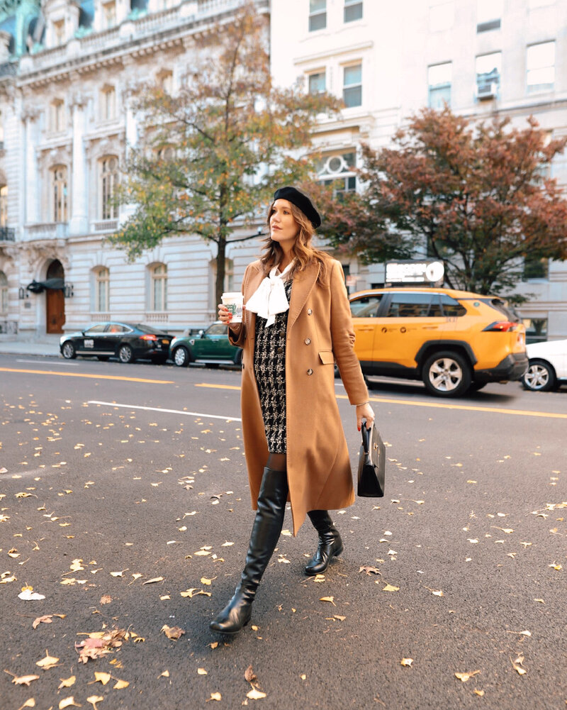 Anna walking across an NYC street wearing a long coat, dress, boots, and beret