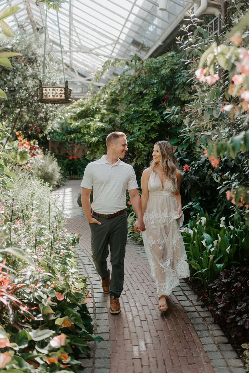 Man and woman stroll hand in hand on a brick paved path through a luscious garden with florals  in a spacious greenhouse in Longwood Gardens in Kennett Square Pa.