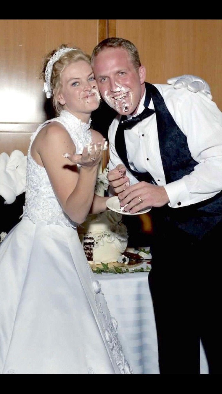 A couple who just got married and did the cake smash at their Disney Wedding with Mickey's hand on the groom's shoulder.