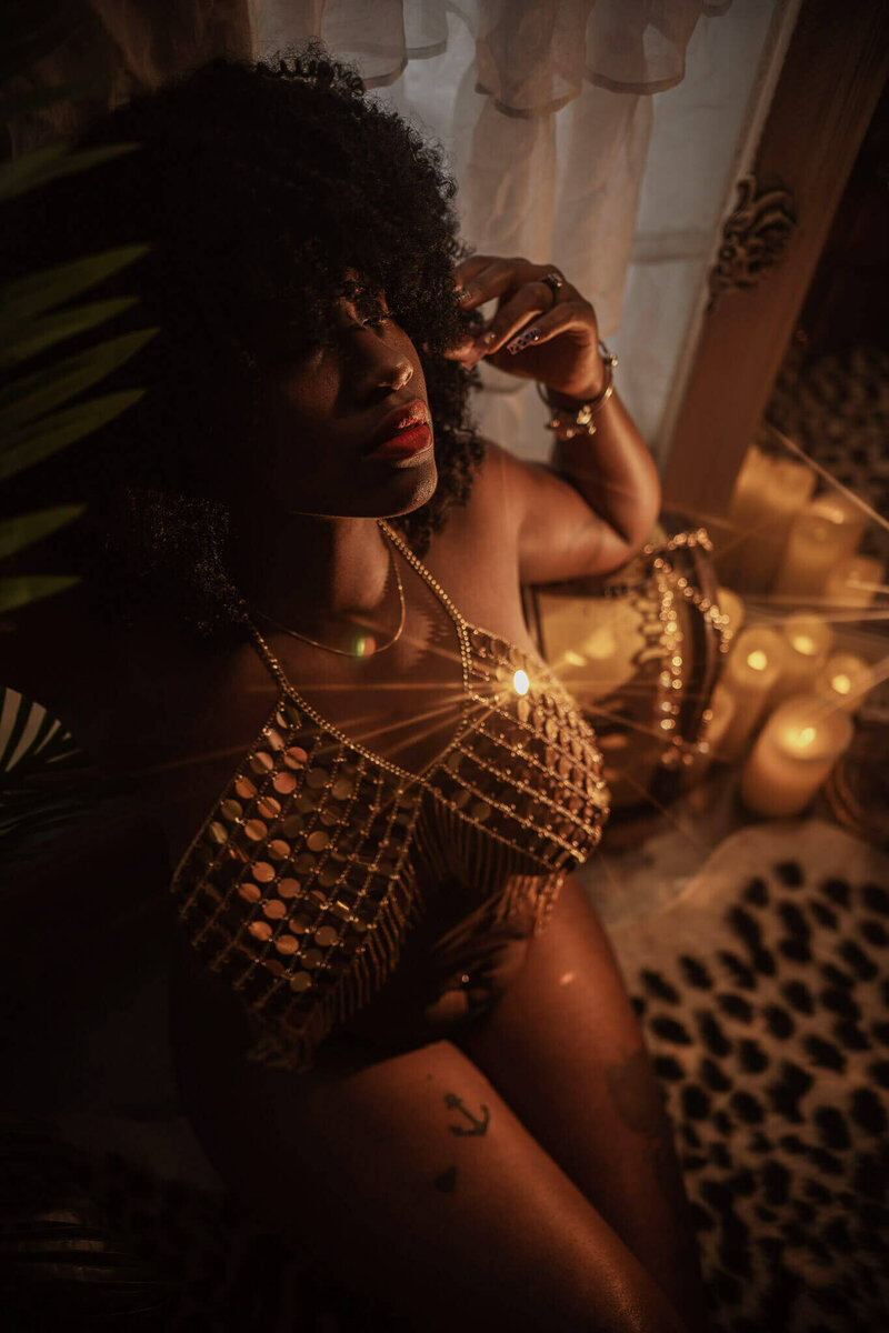 Woman with an afro wearing a gold chain top surrounded by candles.