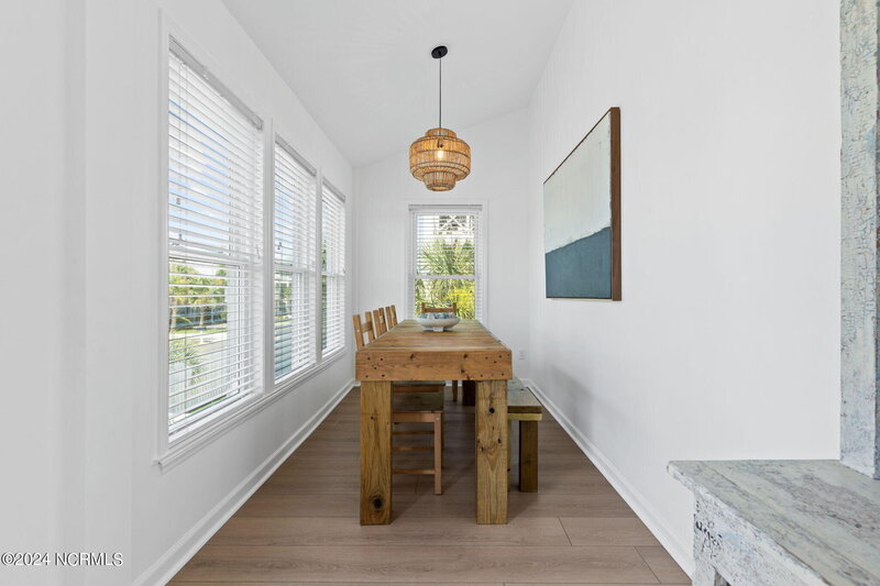 Bright dining room with geometric wooden table, matching bench and chairs, rattan chandelier, and white walls with ample natural light.