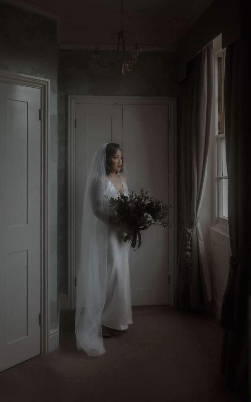Bridal preparations by the window, with the bride holding her bouquet, radiating elegance and grace, moments before walking down the aisle