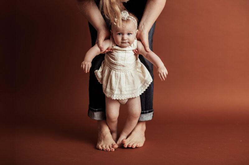vibrant toned studio image of a toddler standing at mother's feet while being held
