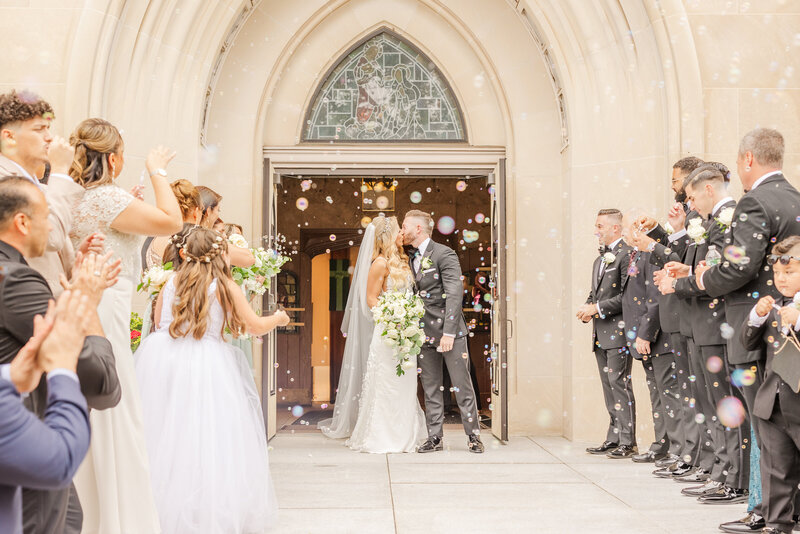 NEwlyweds kiss under a shower of bubbles from their wedding guests at the entrance to the church taken by a Saginaw Wedding Photographer