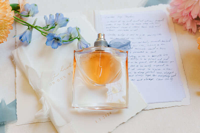 A meaningful flat lay showcasing handwritten wedding vows and perfume beside delicate florals, captured in a soft, romantic style. This image highlights the beauty of faith-filled wedding celebrations, perfect for couples incorporating Christian values into their day. Photographed by a Dallas wedding photographer serving Christian couples across North Texas and beyond.