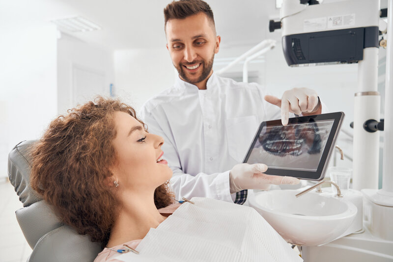 A male dentist showing x-ray photos of teeth to a patient.