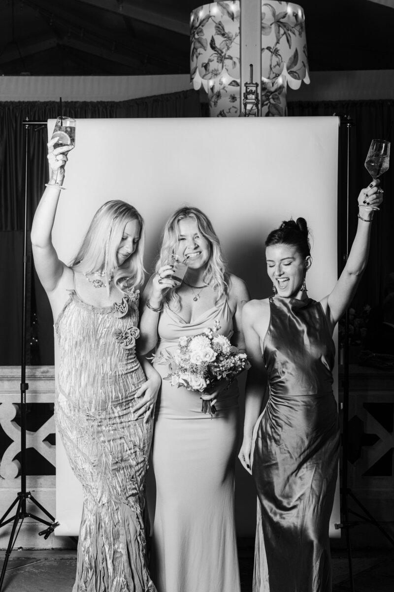 Playful black and white group portrait of three women celebrating with cocktails and flowers at a Vogue Portrait photo booth in Richmond, VA.