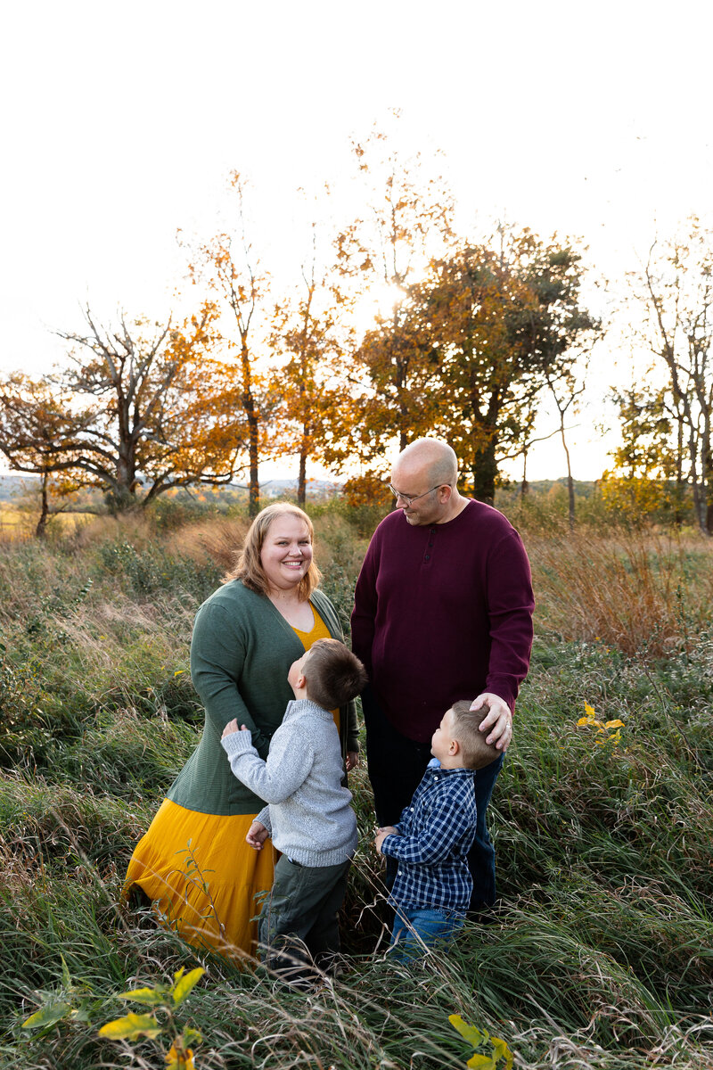 Family of 4 standing in an open field with the sun setting behind them