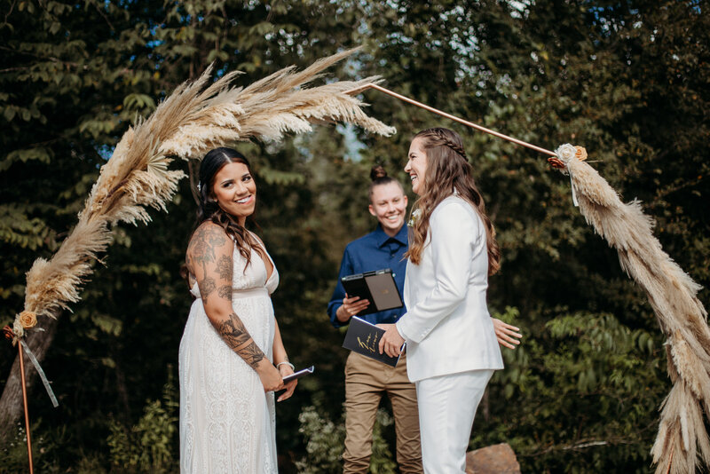 candid outdoor wedding ceremony with a smiling bride in a white lace dress and a bridal party officiated by a person in blue