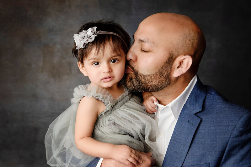 st-louis-family-photographer-toddler-girl-wearing-gray-tulle-dress-being-held-by-dad-wearing-blue-suit