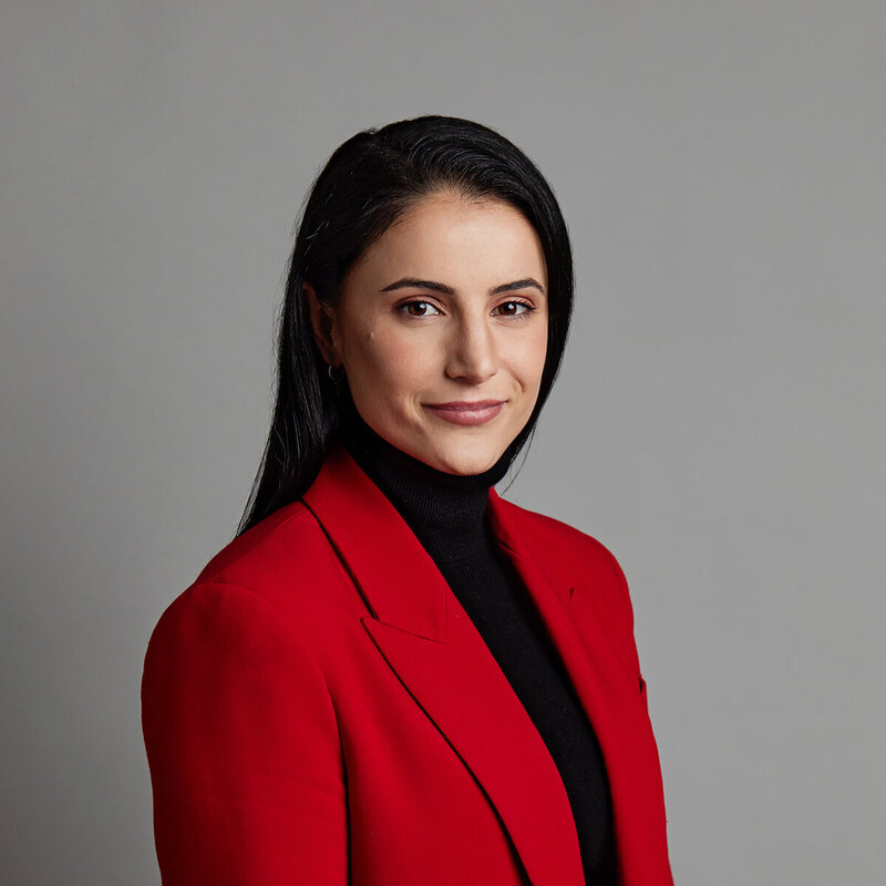 Woman in a red jacket and long dark hair against a grey background.