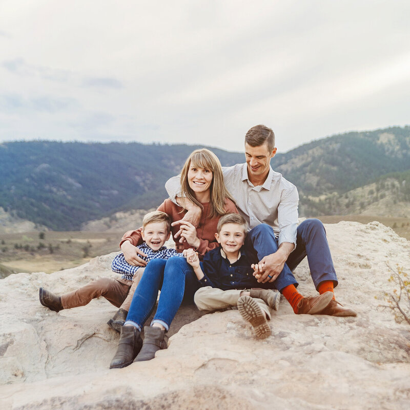 colorado family of four sitting on rocks above reservoir on beautiful cloudy day