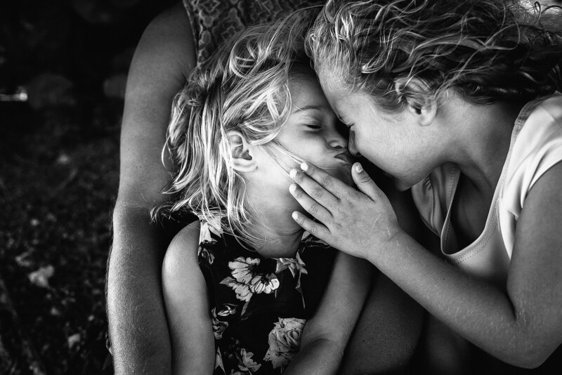 Black and white portrait of sisters giving Eskimo kisses at beach in Florida.