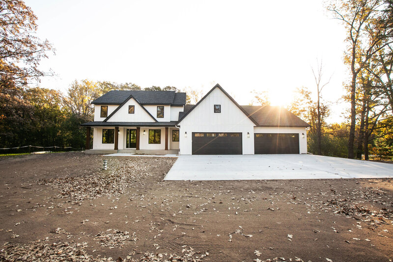 Custom cream home in Big Lake Township by Cornerstone Custom Builds with cream siding, wood pillars and black finishes.