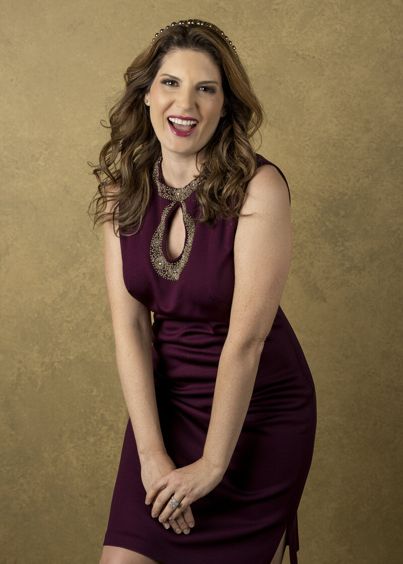 Melanie Herschorn smiling in a black dress against a gold background