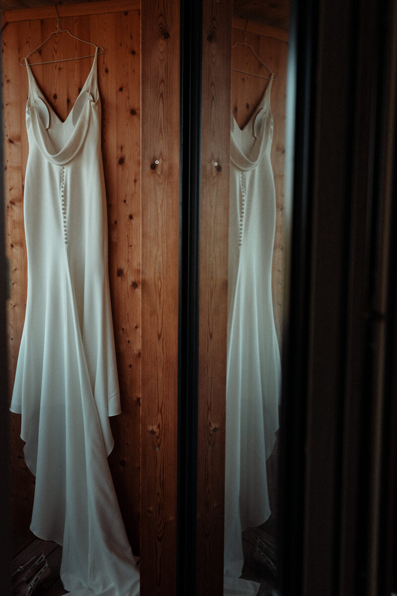 Elegantes Hochzeitskleid vor einer Holzwand, das sich in der Türe spiegelt.