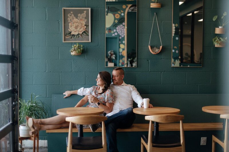 Two people sitting and relaxing in a modern café with green walls and wooden furniture, often chosen by the best destination photographers for casual photoshoots.