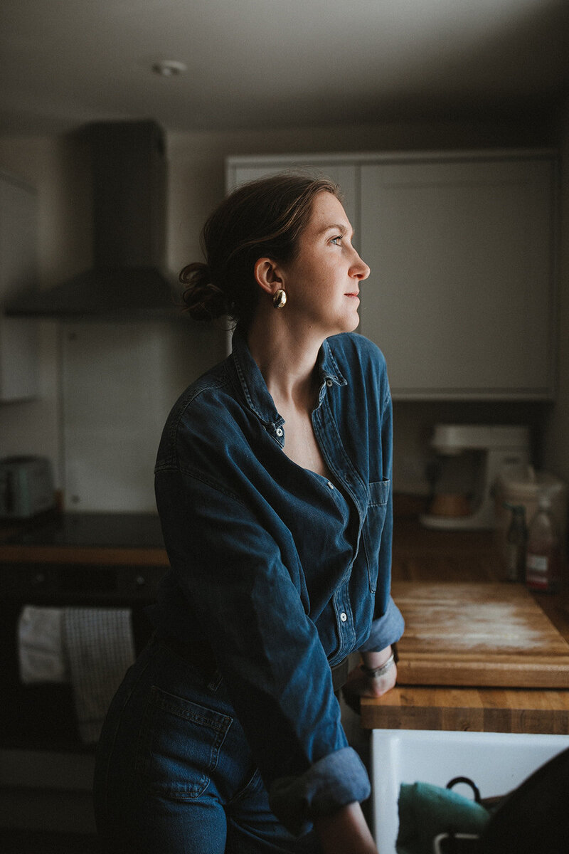 Business coach looks out of the window of her Oxfordshire home in a stylish outfit