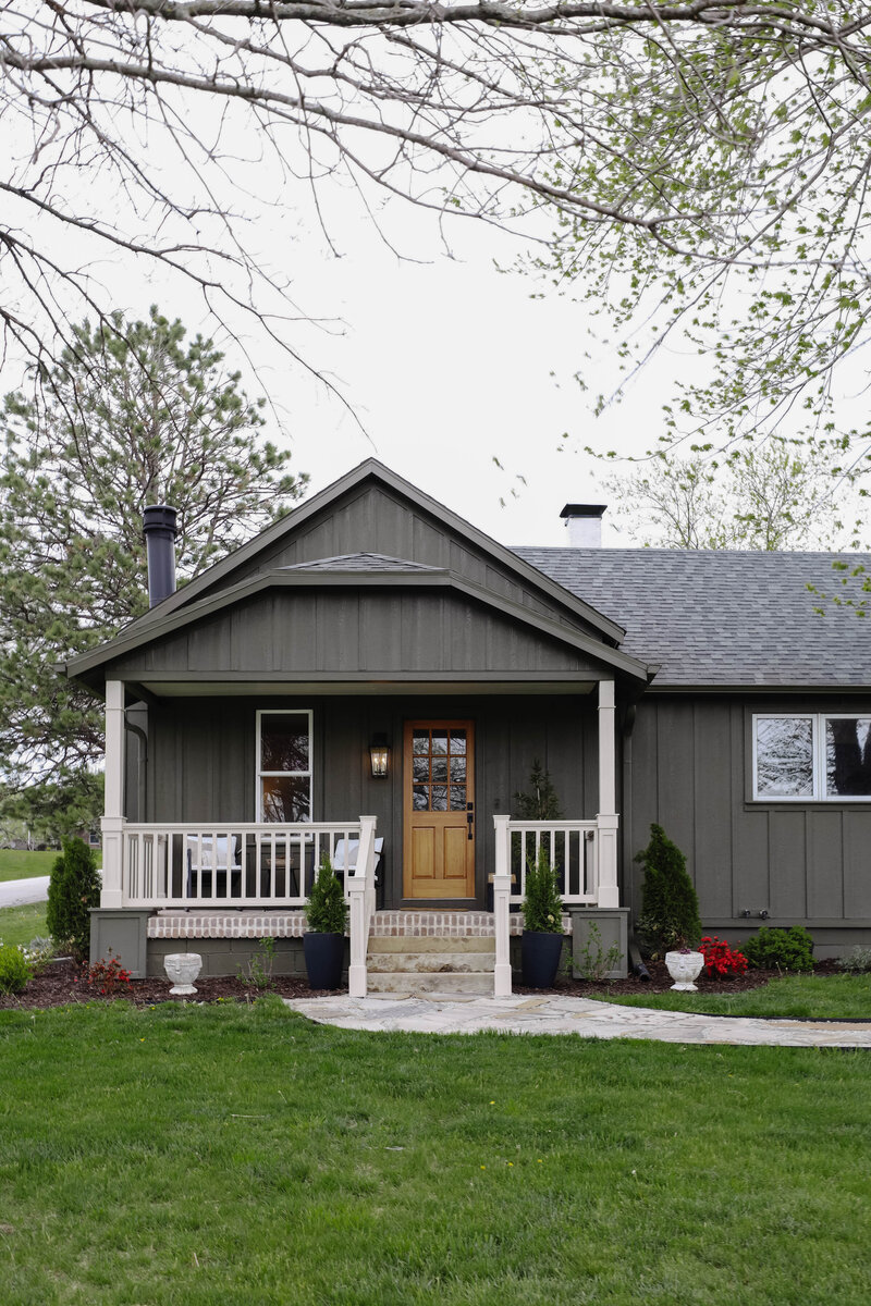 The exterior project by Nadine Stay. Board and batten siding install. Muddled Basil by HGTV Home by Sherwin Williams exterior paint color. Flagstone path, brick front porch floor, and a custom built railing. Cabin exterior.