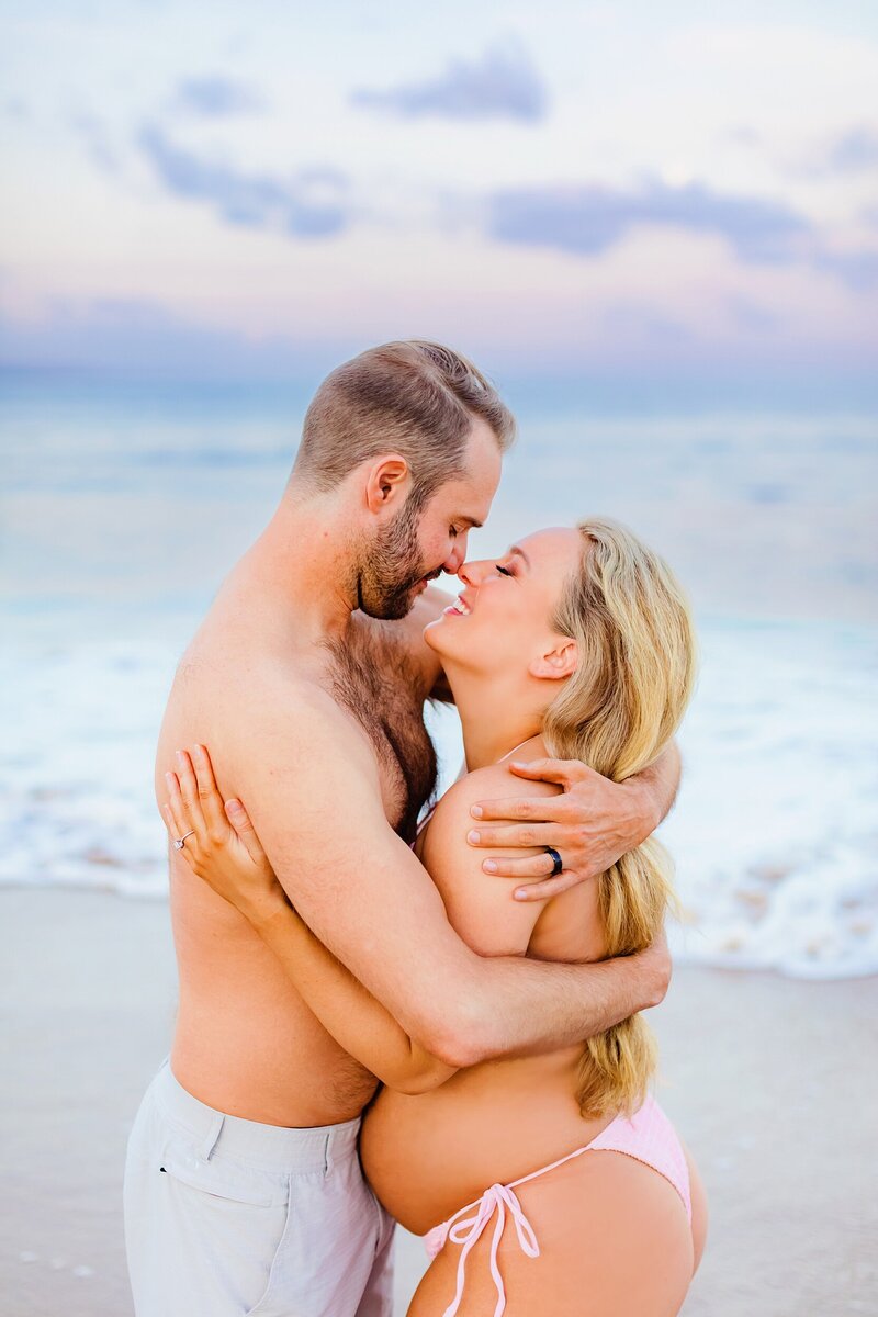 Beautiful pregnant woman photographed by Love + Water on Maui holds her belly and stares out to sea