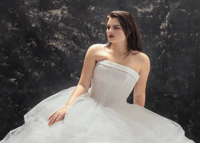 lady in white wedding gown seated facing sideways in front of a rough dark textured studio wall