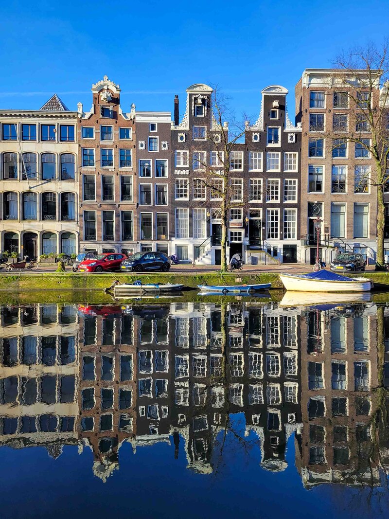 Historic canal houses with ornate gables reflected in the water on a sunny day in Amsterdam, Netherlands ©Stephanie Dosch | theViatrix Luxury Travel
