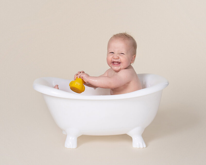 Baby splashes in tiny tub at his first birthday  session with Laura King Photography