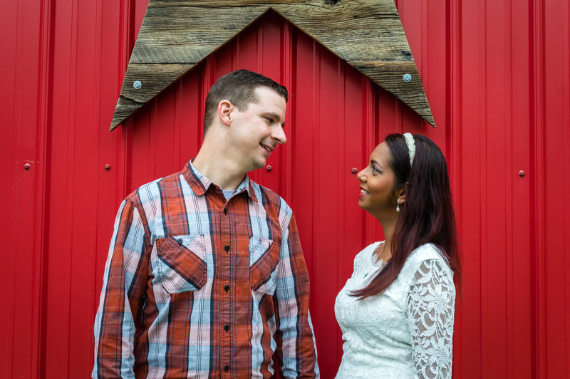 Engaged couple poses at a park in front of wooden fence