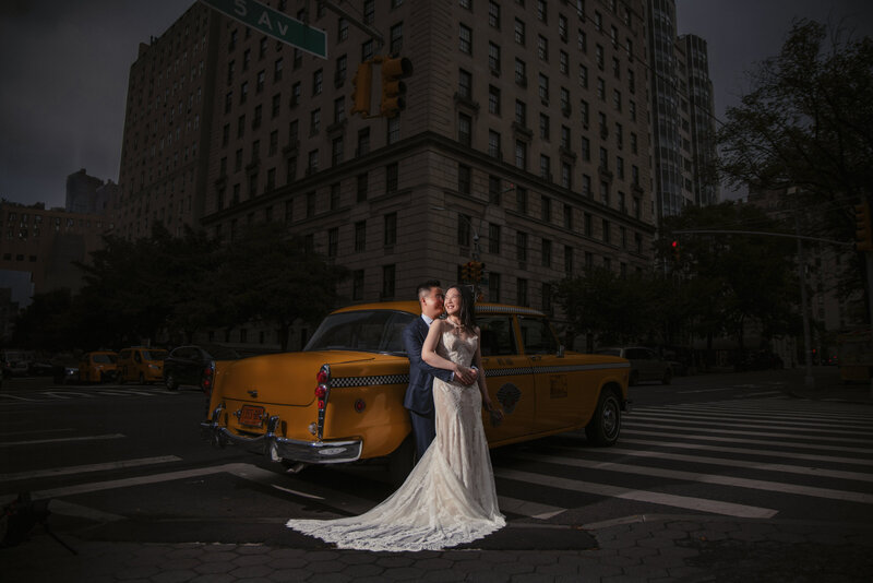 A wedding couple with their arms around each other leaning on a vintage cab.