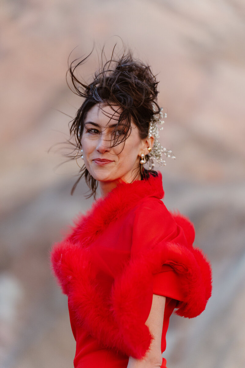A woman in a cherry red dress and shawl looks over her shoulder.
