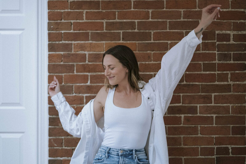 Confident and authentic yoga and pilates instructor in a relaxed pose with her arms raised against a brick wall