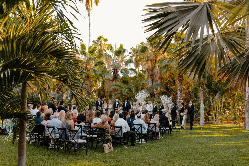 Wedding ceremony at Acre Resort with palm trees, tropical greenery, and guests seated outdoors.