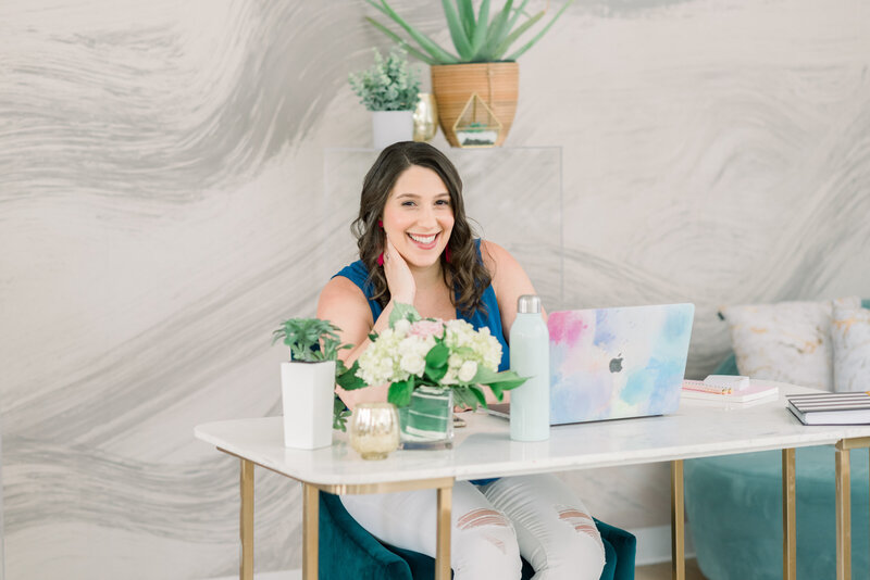 Isabel Kateman, a website strategist and copywriter, sitting at a desk wearing white jeans and a blue top.