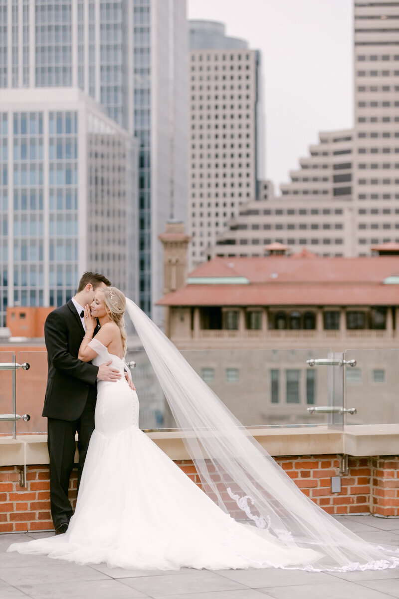 Bride and groom hugging on a rooftop with a cathedral veil