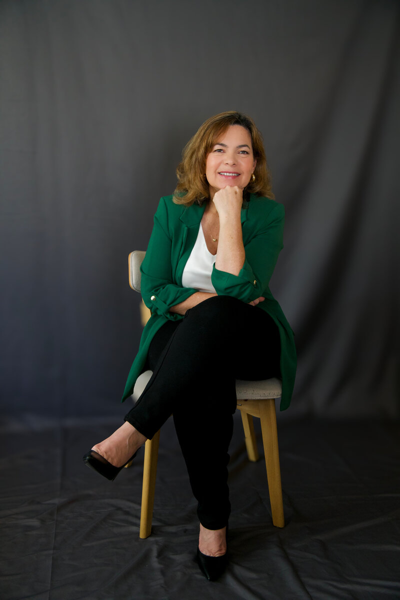 Brazilian woman sitting in a chair in front of a black backdrop smiling at the camera
