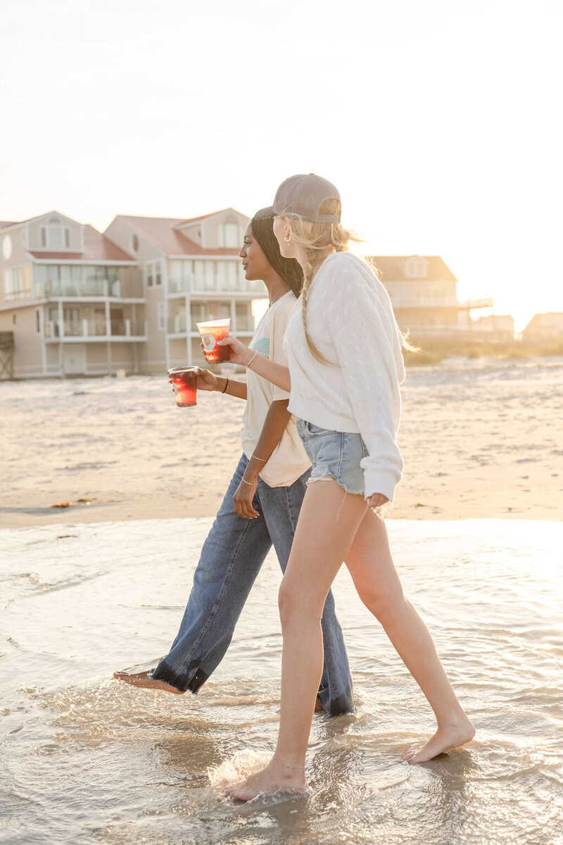 two baristas walk barefoot in the ocean holding their iced teas from sundial coffee and tea