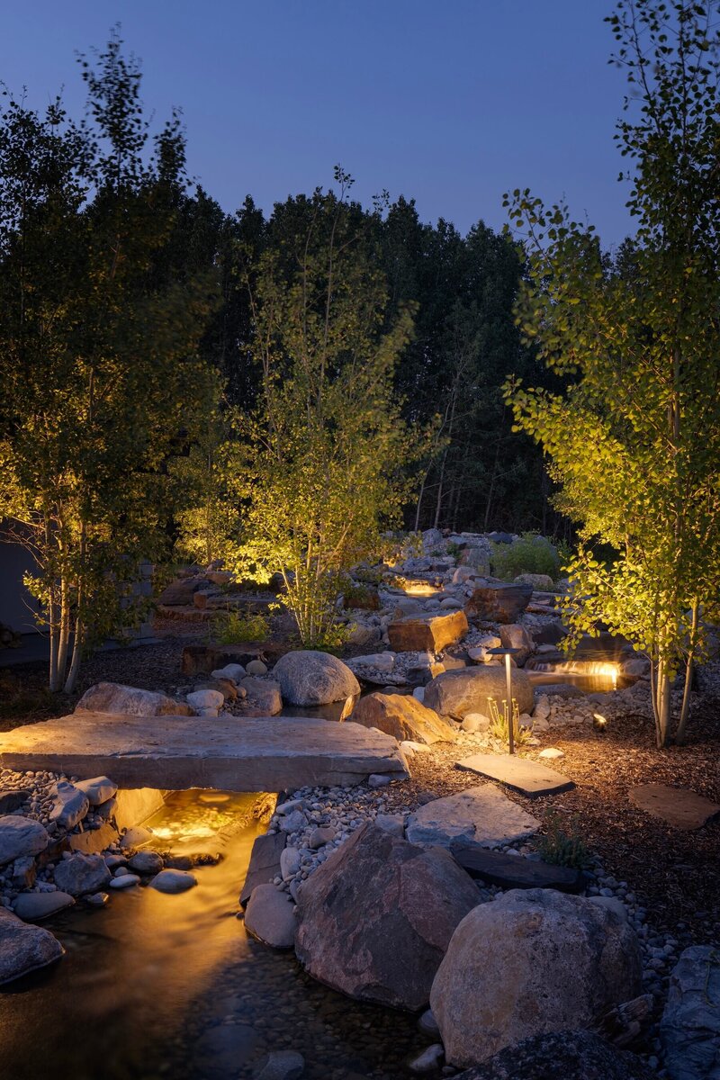 A bacykard oasis with a moat and floating stream, big trees and outdoor accent lighting. 