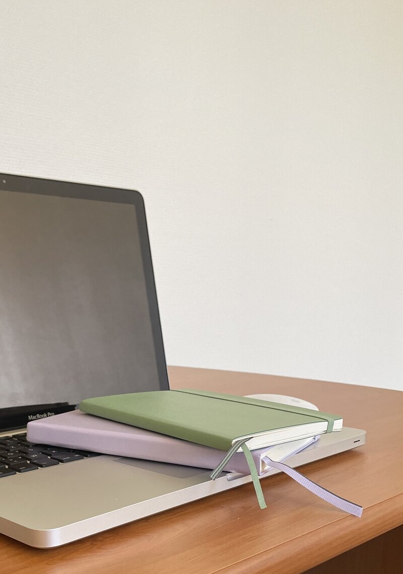Deux carnets (un vert sauge et un lilas) sont posés sur le clavier d'un ordinateur portable