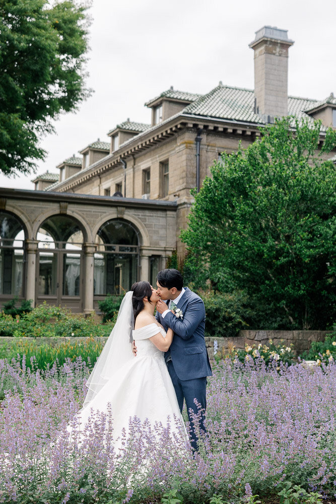 Contact | Newport and CT Wedding Photography & Videography | Light and Airy | Couple kissing with a mansion behind them in front of lavender bush.