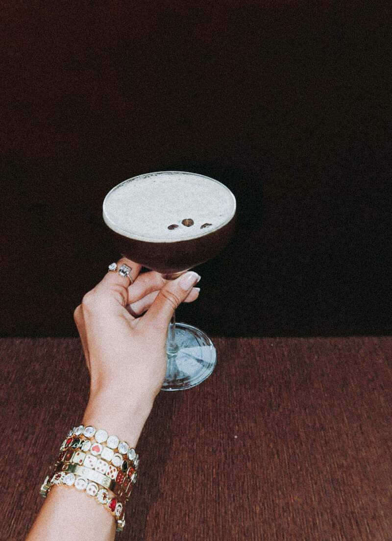 espresso martini being held by womans hand with ring