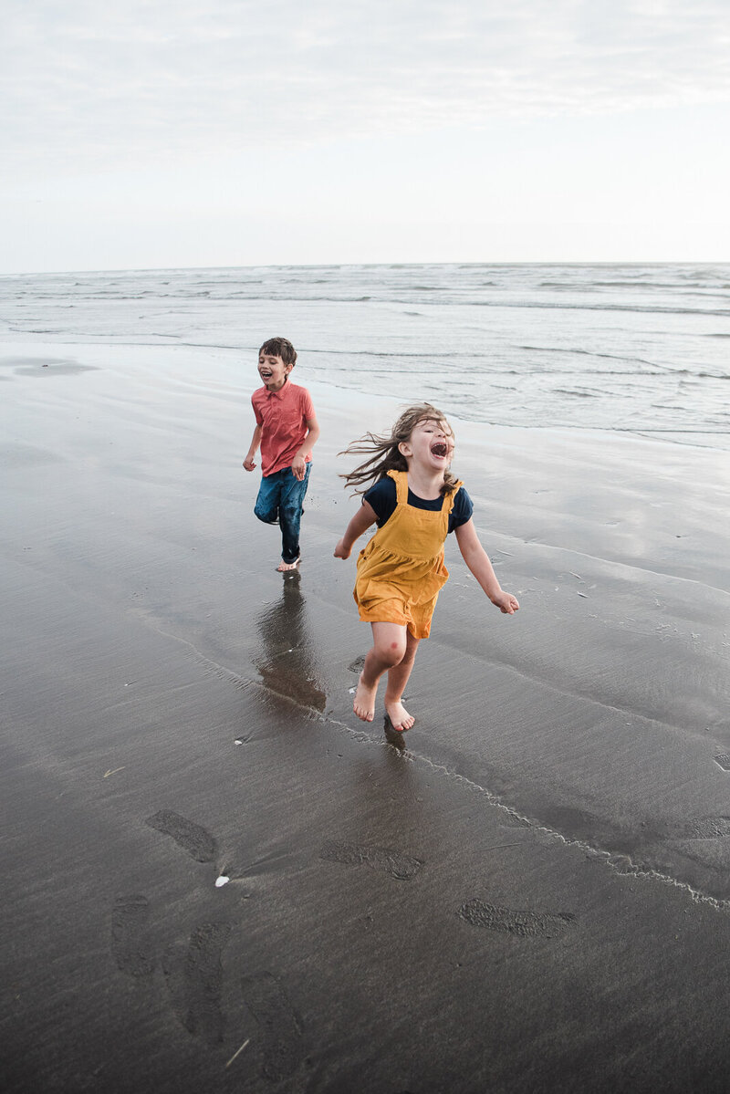 Brother and sister running in the surf during their family adventure photo session at Pacific Beach WA near Seabrook