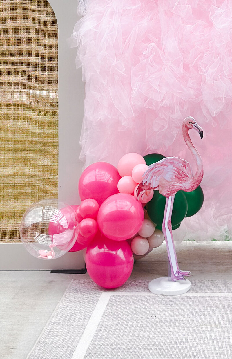 Pink and green balloons with a flamingo in front of a pink tulle wall.
