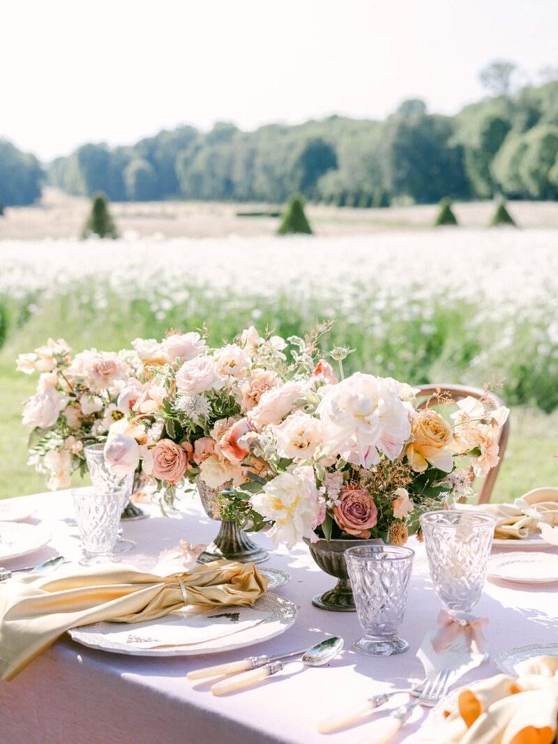 Floral table centerpieces on outdoor wedding table with silverware, glasses, and plates