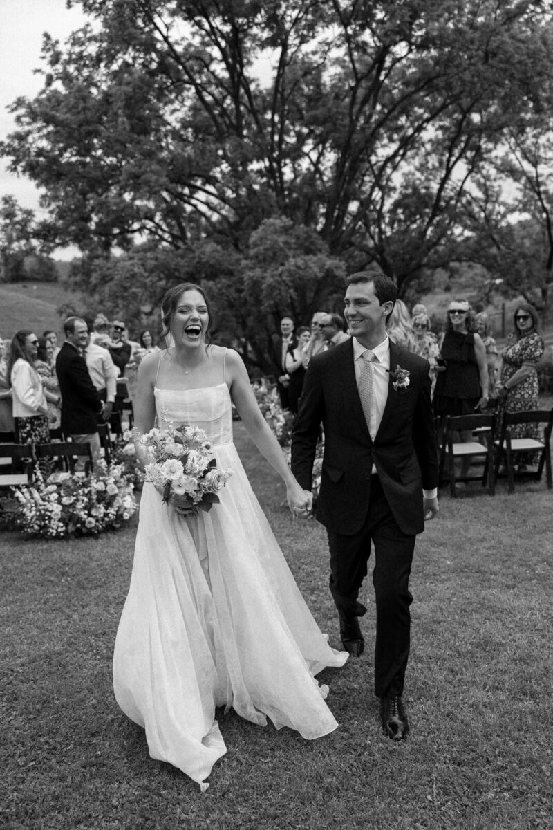 Bride and groom holding hands and joyously walking back up the aisle as husband and wife in the mountains of Asheville, NC, captured by Andrea-Marie Photography