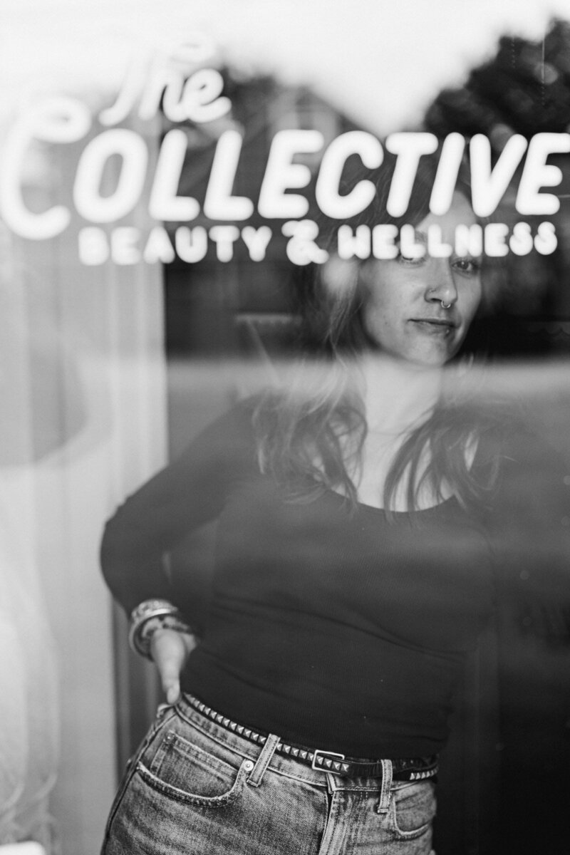 Hair stylist Chelsea is viewed through a glass window with the Words The Collective Beauty and Wellness visible above her.