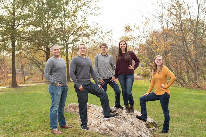 Adult siblings standing on rock with autumn trees behind them