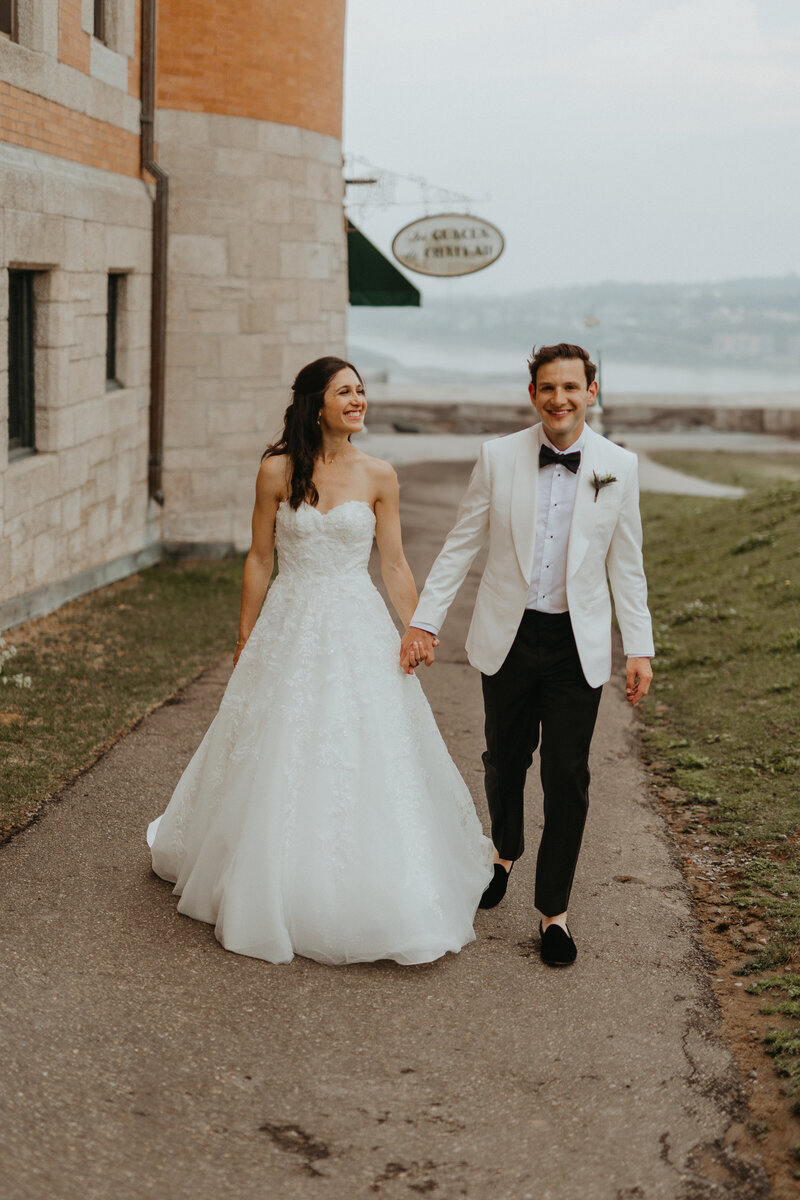 Experience love in Quebec: newlyweds walking near Château Frontenac, with the St. Lawrence River in the background. A radiant image of happiness and natural beauty.