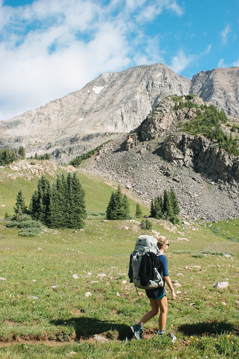 Libby Stenzel, RDN, backpacking with a large backpack with rocky terrain the background.